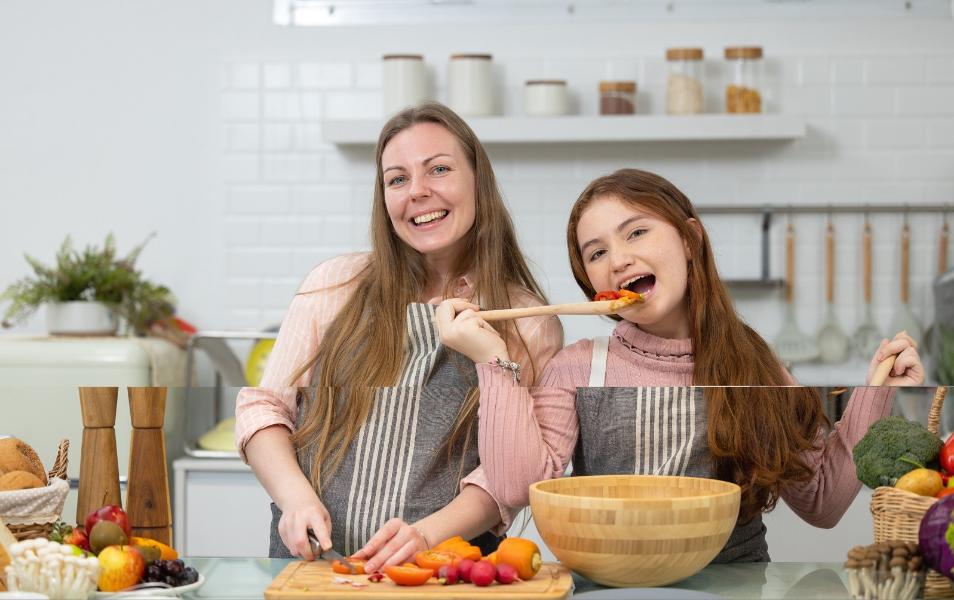 In a white, spotless modern kitchen, a smiling mother and daughter demonstrate how to prepare veggies for dinner.