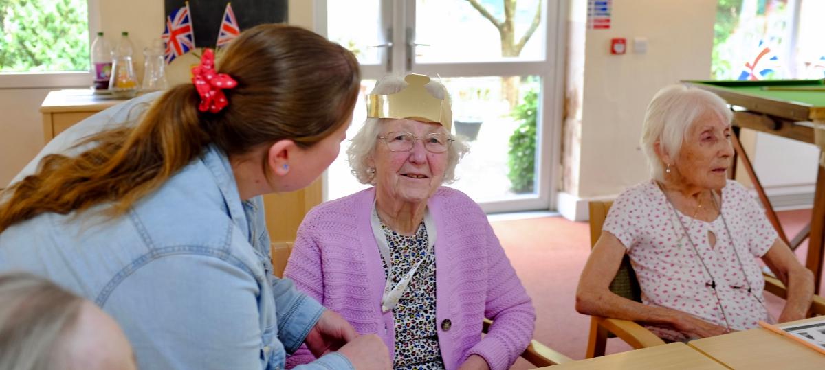An older lady sat talking to another lady in a dinning room.