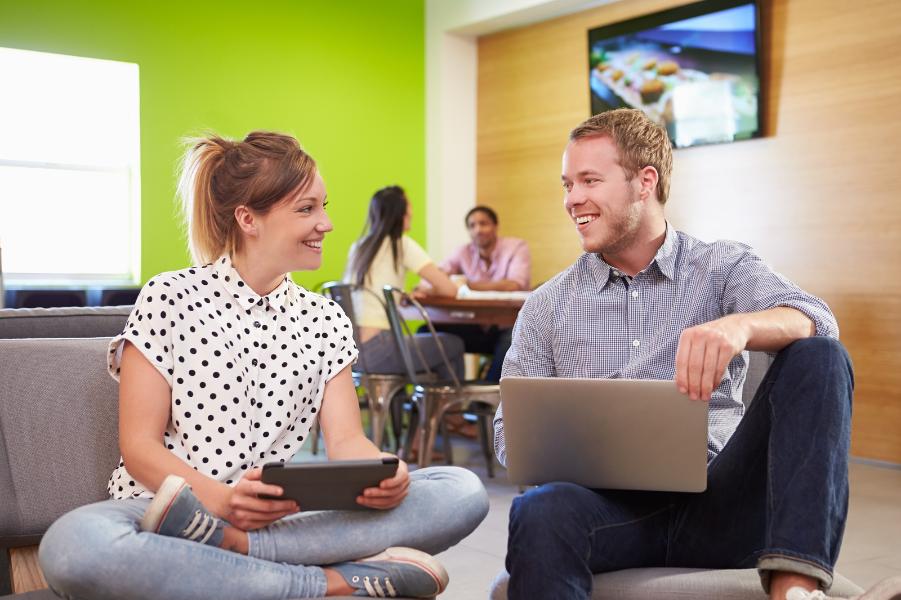 Young people sat on the floor looking at each other holding a tablet and a laptop